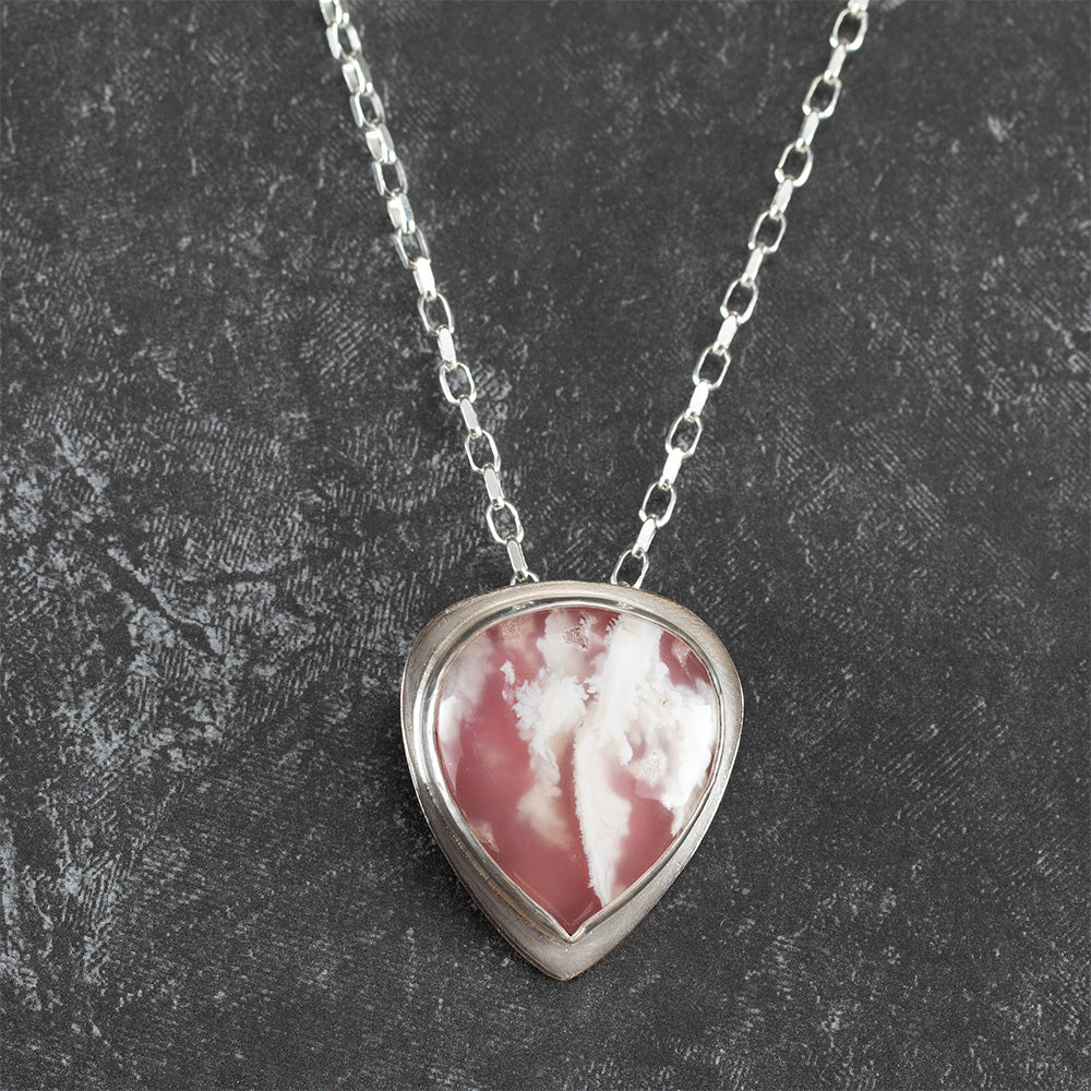 Sterling silver necklace featuring a teardrop-shaped pink and white plume agate stone, bezel set on a textured chain – handcrafted petal-inspired design by Divella Designs.