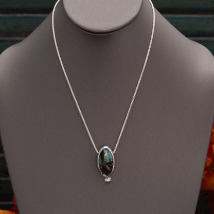Sterling silver necklace with a marquise-shaped purple mohave stone pendant displayed on a gray stand with autumn leaves in the background.