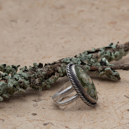 Rainforest Jasper ring on bark with lichen covered branch in the background