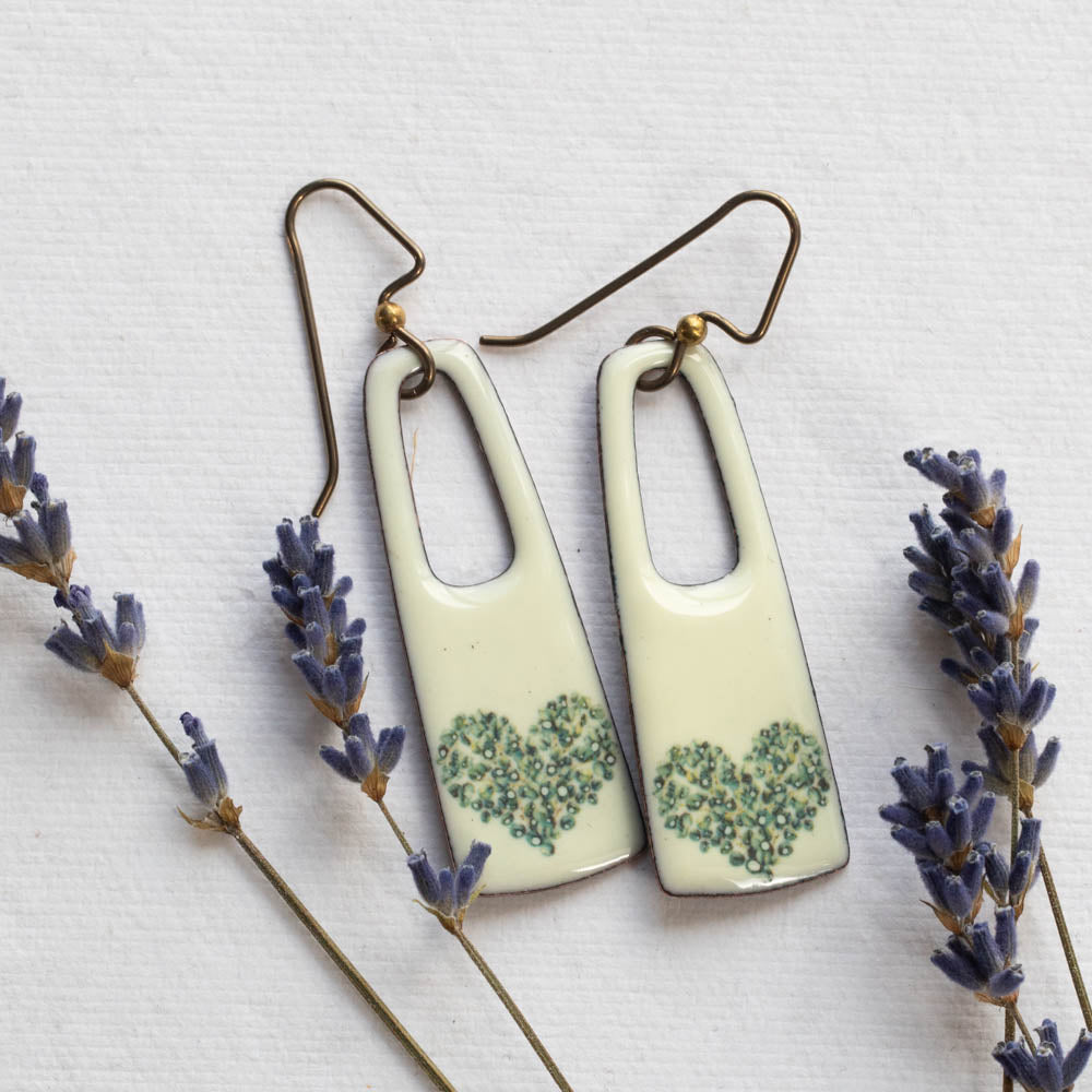 Pair of enameled copper earrings with floral design on a white background with lavender flowers.
