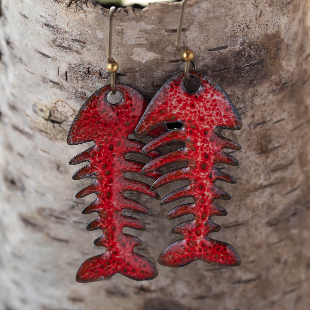 Red and black fish skeleton earrings on a wooden background