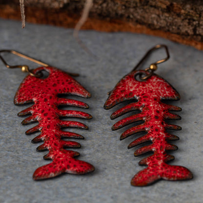 Red fish bone-shaped earrings on a textured surface