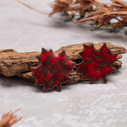Red maple leaf-shaped earrings on a wooden branch with a natural background