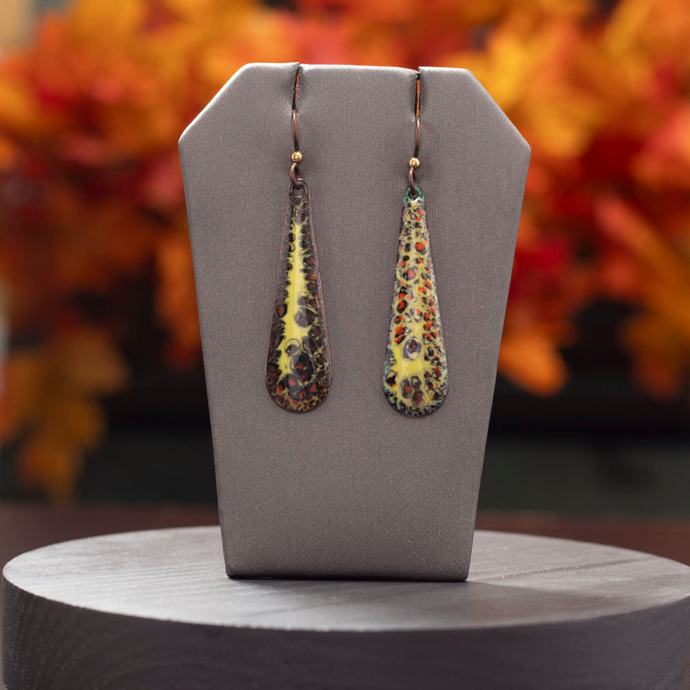 Brown, orange, and yellow enamel teardrop earrings displayed with autumn leaves on a dark background.