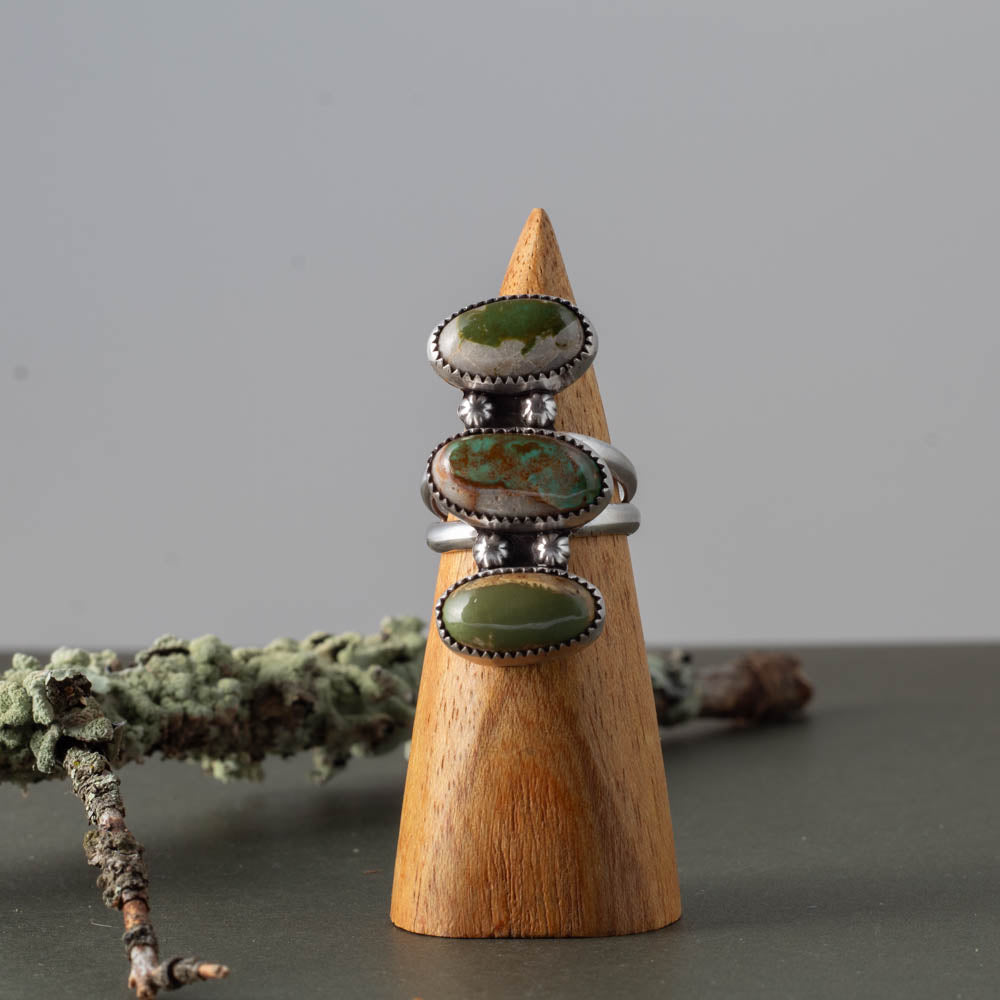 Three Royston turquoise stone rings on a wooden cone with a natural background