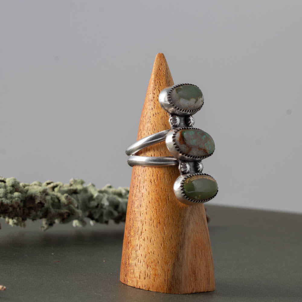 Silver ring with royston turquoise gemstones on a wooden cone against a gray background