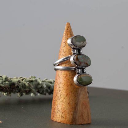 Silver ring with royston turquoise gemstones on a wooden cone against a gray background