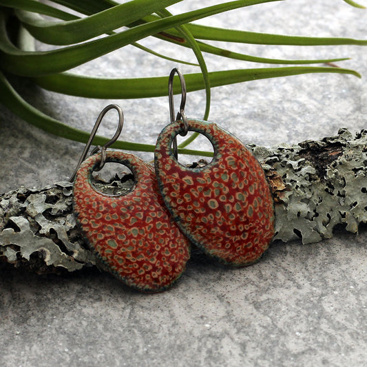 Handcrafted oval dangle earrings with fiery red and earthy green kiln-fired enamel on copper and niobium ear wires.