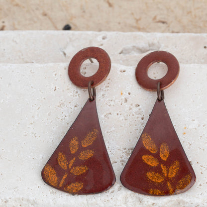 Pair of brown earrings with leaf patterns on a textured surface