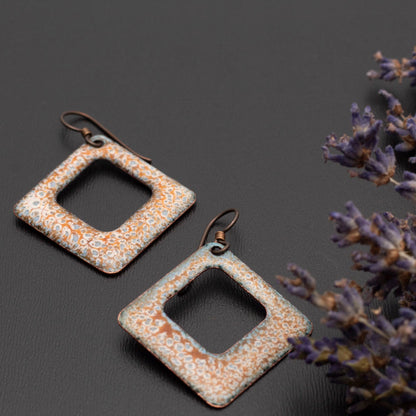 Square copper enamel earrings with soft sage green, rust, and ivory crackle glaze, displayed on a dark background with sprigs of dried lavender.