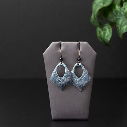 Diamond-shaped enamel earrings with a smoky blue and white speckled pattern, featuring an open teardrop center and niobium ear wires with faceted gemstone beads.
