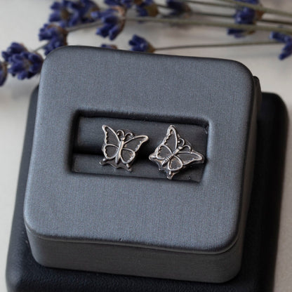 Sterling silver butterfly stud earrings displayed on a gray jewelry box, with sprigs of dried lavender in the background.
