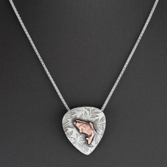 Handcrafted sterling silver pendant with etched floral background and raised copper jumping bass fish, hung on a silver chain – rustic nature-inspired necklace by Divella Designs, displayed on dark background.