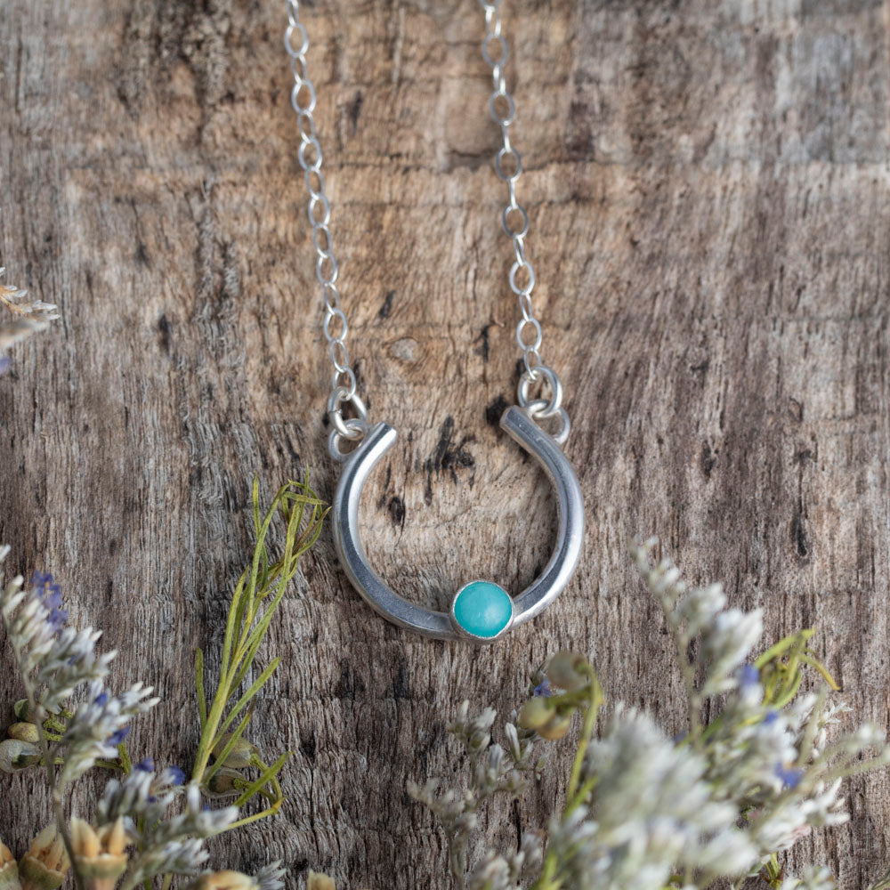 Silver necklace with a amazonite stone on a wooden background with plants