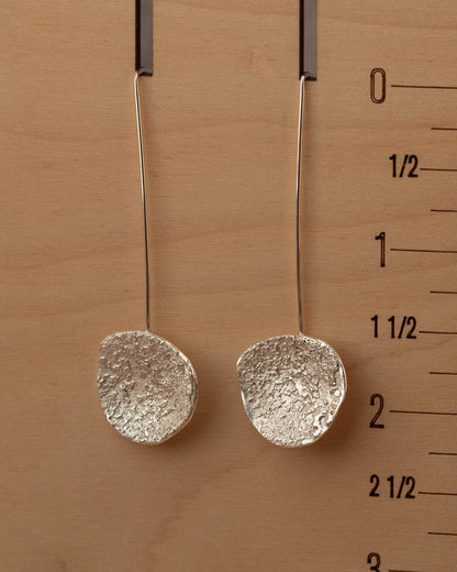 Textured sterling silver dangle earrings resting on rustic wood, showcasing handmade craftsmanship by Divella Designs Jewelry.