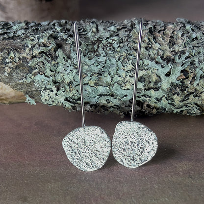 Silver textured earrings on a stone surface