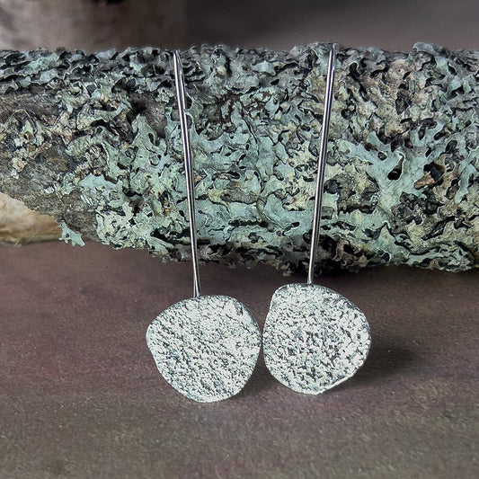 Silver textured earrings on a stone surface