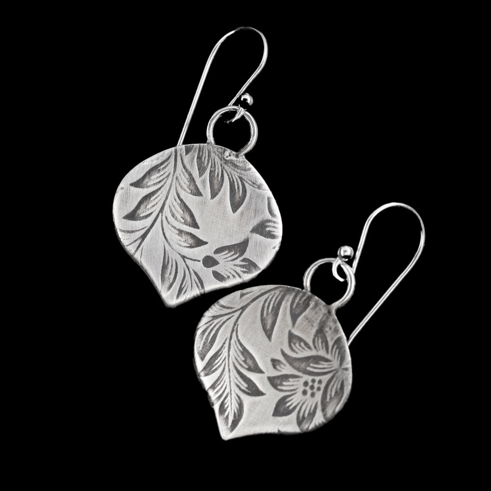 Handcrafted sterling silver earrings with etched botanical leaf and flower pattern, soft matte finish and organic shape – artisan nature-inspired jewelry by Divella Designs, shown on black background.