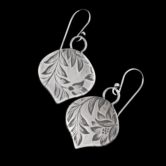 Handcrafted sterling silver earrings with etched botanical leaf and flower pattern, soft matte finish and organic shape – artisan nature-inspired jewelry by Divella Designs, shown on black background.