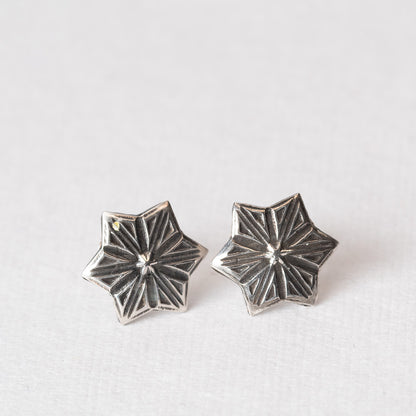 Pair of handcrafted sterling silver star-shaped stud earrings with etched radiating lines, displayed on a light fabric backgroun