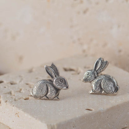 Pair of silver rabbit earrings on a textured beige surface