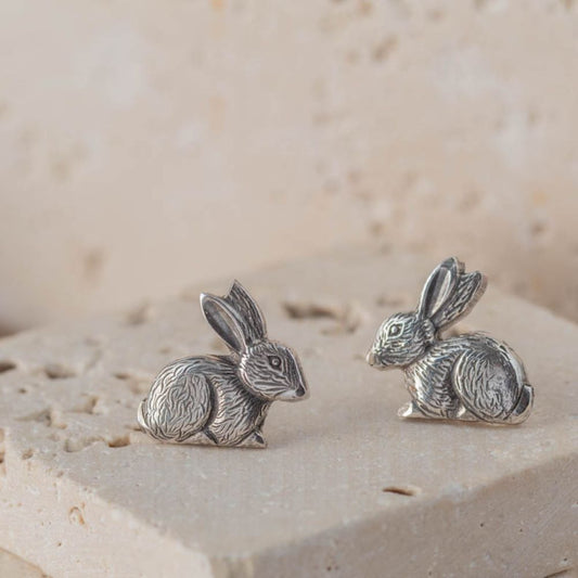 Pair of silver rabbit earrings on a textured beige surface