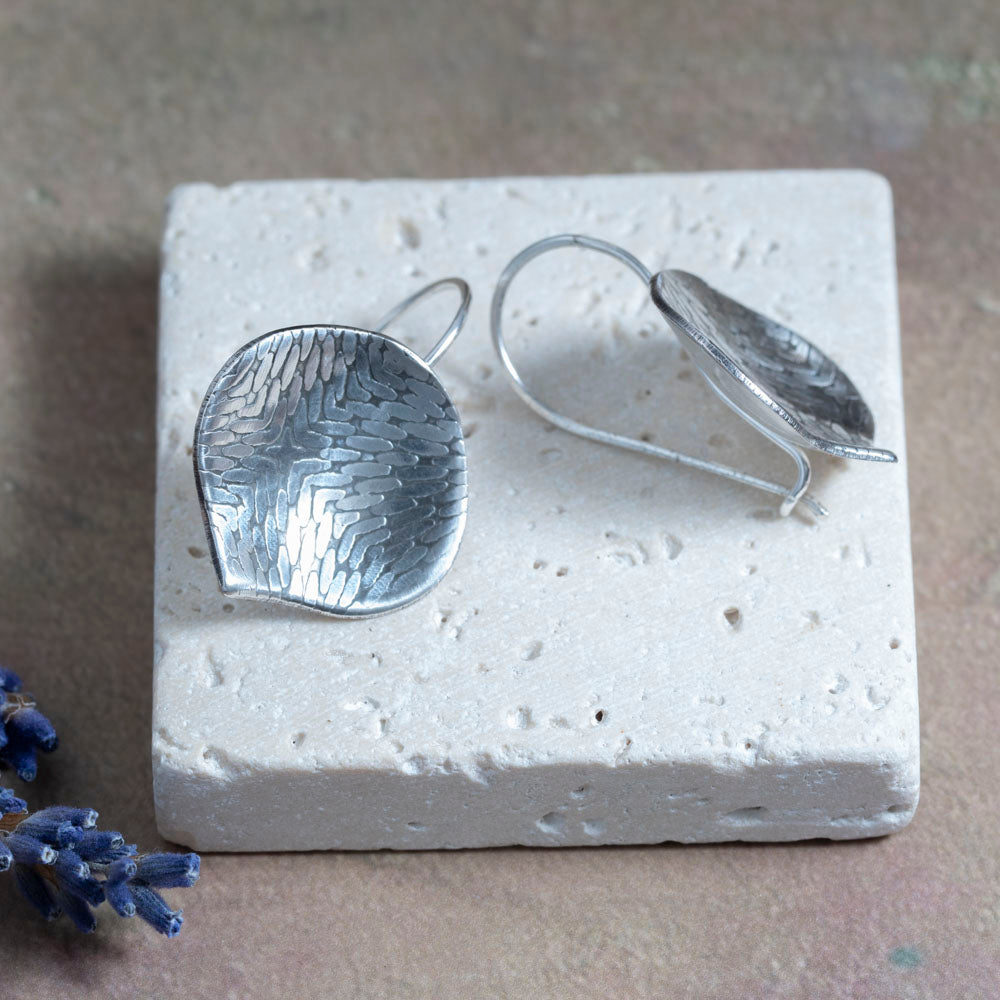 Silver earrings showing the catch in the back on a textured white stone surface with a blurred background