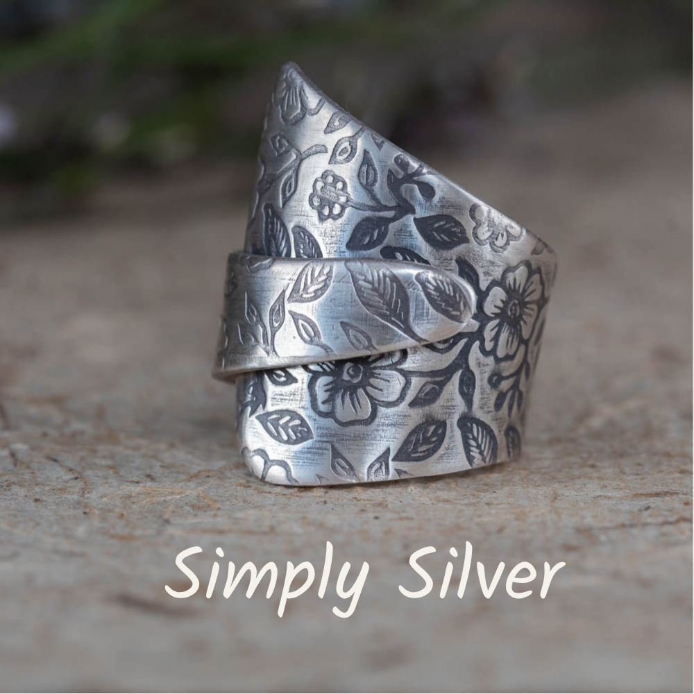 Silver ring with floral patterns on a textured surface, labeled 'Simply Silver'.