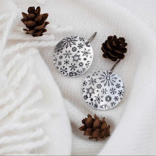 Pair of earrings with floral patterns on a white fabric background with pine cones.
