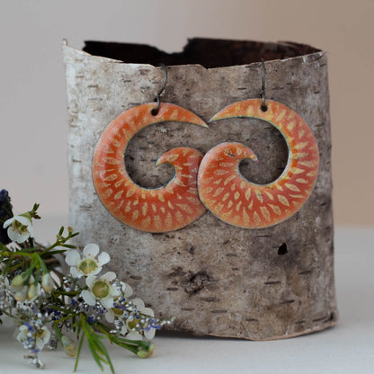 Bright orange and yellow spiral enamel earrings with sunburst floral pattern, nature-inspired artisan jewelry by Divella Designs."