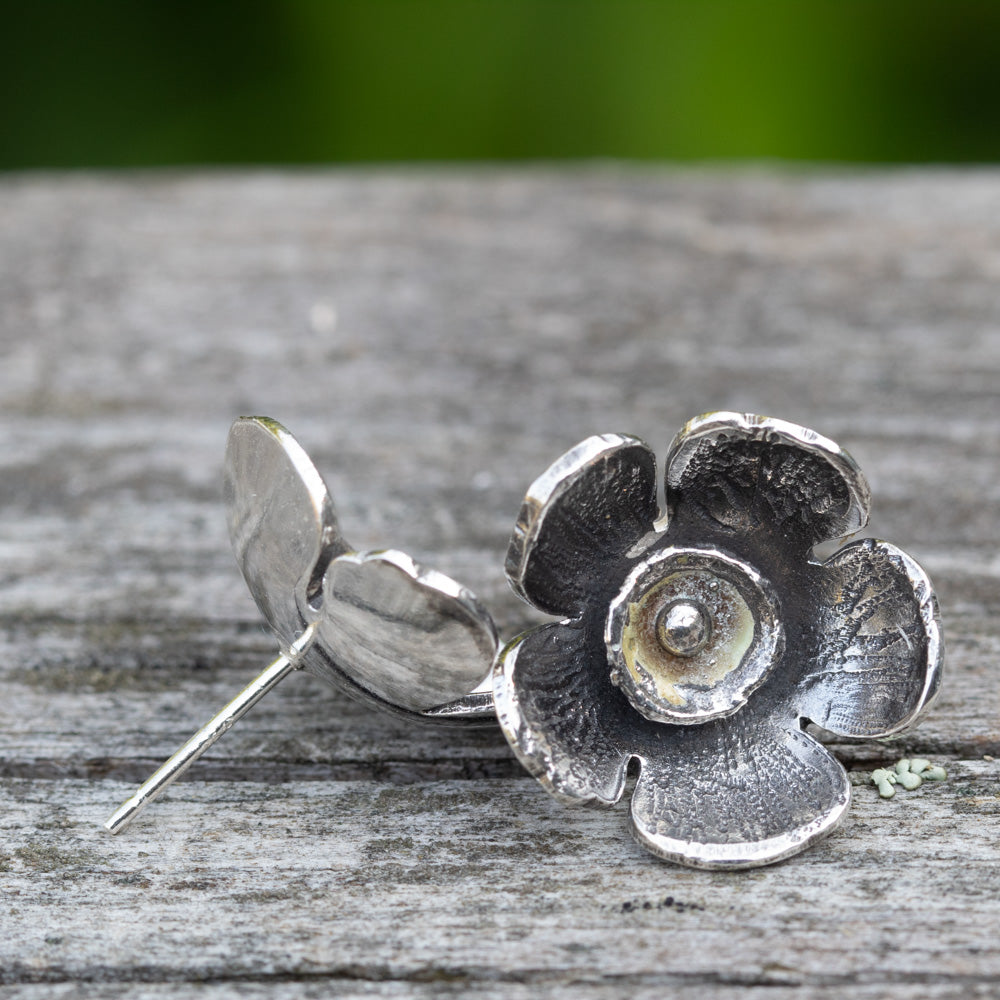 Silver flower-shaped earring on a wooden surface with a blurred green background