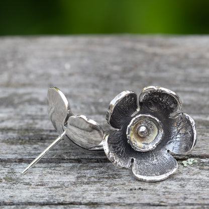 Silver flower-shaped earring on a wooden surface with a blurred green background