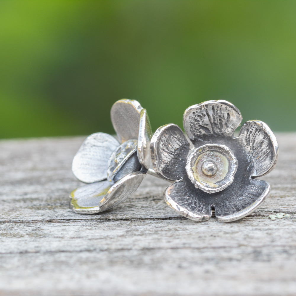 Silver flower-shaped earrings on a wooden surface with a blurred green background