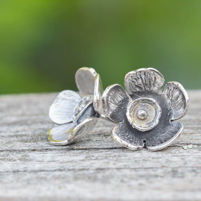 Silver flower-shaped earrings on a wooden surface with a blurred green background