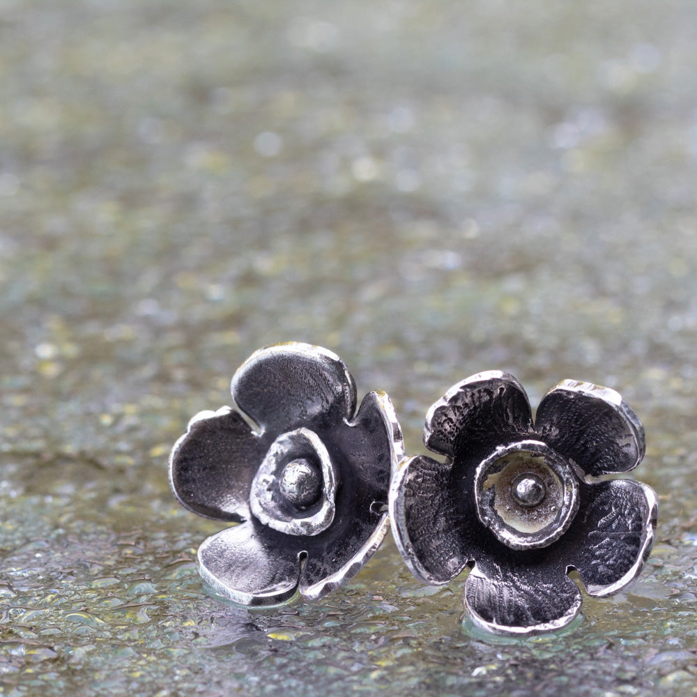 Pair of silver flower-shaped earrings on a textured surface