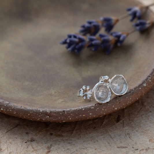 Silver stud earrings on  ceramic dish with lilacs in the background