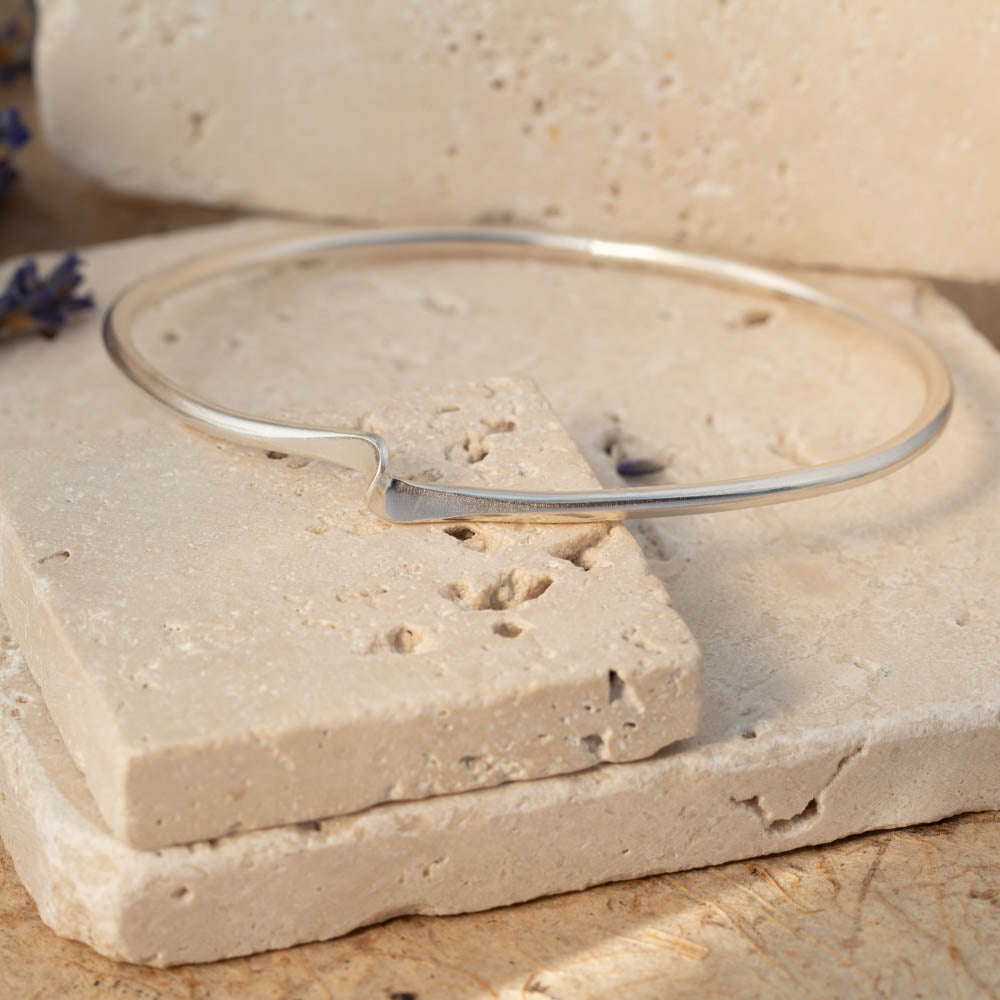 Silver bangle on a textured stone surface with lavender flowers