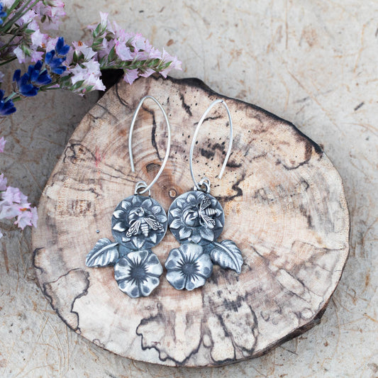Sterling silver bee and flower dangle earrings with layered blossoms, textured leaves, and soft patina, handmade in Vermont by Divella Designs.