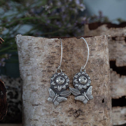 Sterling silver butterfly and flower earrings by Divella Designs, 2-inch dangle with leaf and petal detail, handmade in Vermont and photographed on birch bark
