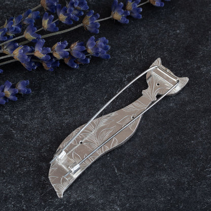Back of handcrafted sterling silver cat brooch with a minimalist, elongated design and abstract facial features, displayed on a textured black background