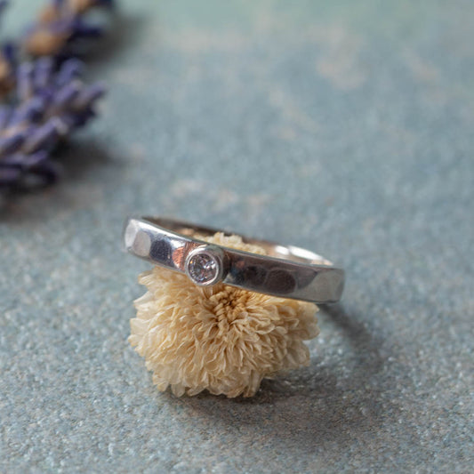 Handmade silver ring with small CZ set in smooth tube setting on soft blue surface with dried flower