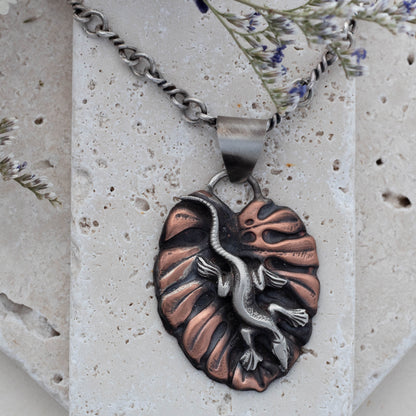 Close up of handmade copper pendant necklace featuring a sculpted lizard on a textured leaf background, with oxidized finish and nature-inspired artisan design.