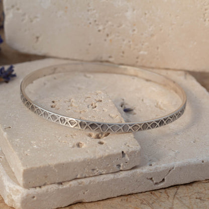 Silver bracelet with geometric pattern on a textured stone surface