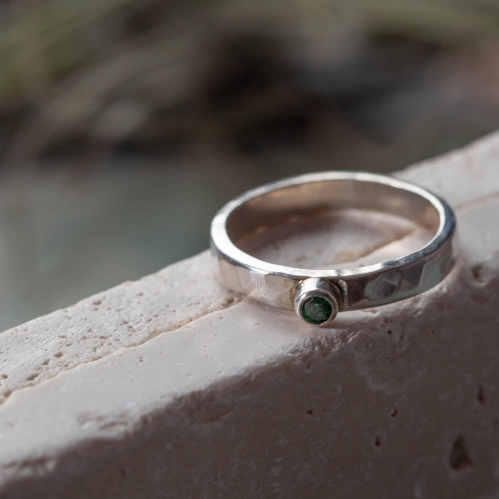 Sterling silver hammered ring with green cubic zirconia on neutral textured background