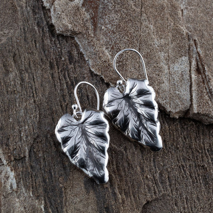Sterling silver leaf dangle earrings with detailed vein texture and heart-shaped foliage design, displayed on natural rustic wood background.
