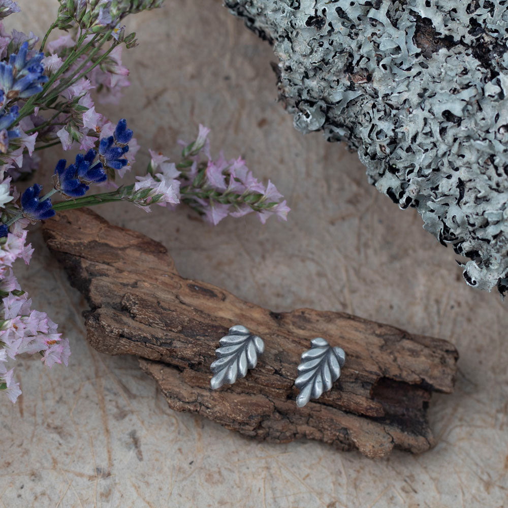 Sterling silver leaf stud earrings by Divella Designs, handmade in Vermont with satin finish, styled on bark with lichen and wildflowers