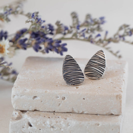 Handmade sterling silver teardrop stud earrings with etched line texture, featuring a minimalist nature-inspired design and oxidized finish.