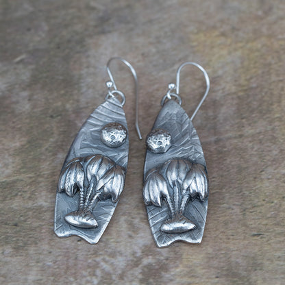 Handcrafted sterling silver earrings featuring sculpted willow trees under a textured full moon on leaf-embossed backdrops – Moonlight Surfing nature-inspired earrings by Divella Designs, shown on earthy background.
