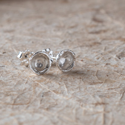 Silver stud earrings on a textured beige surface