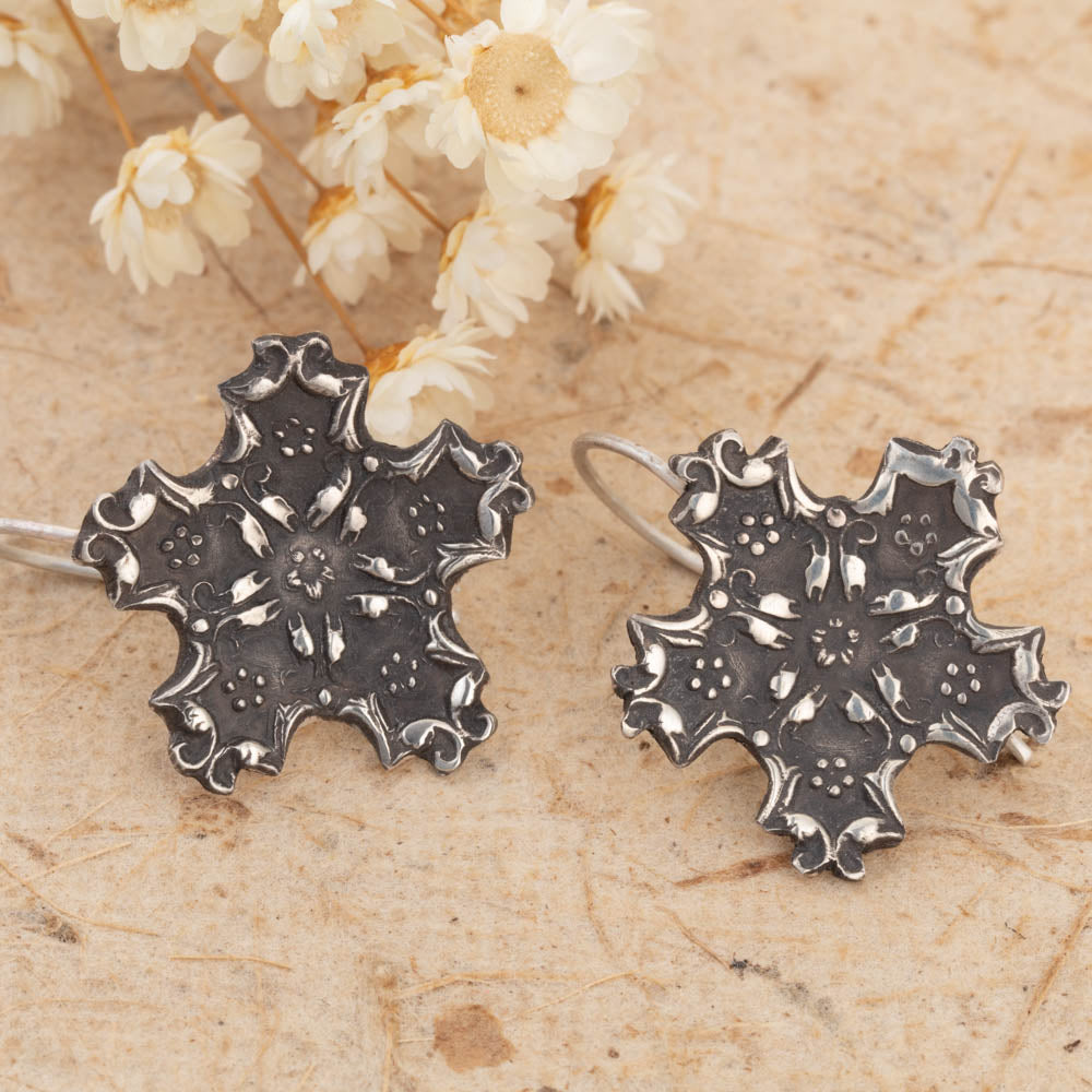 Silver snowflake earrings on a textured surface with dried flowers in the background